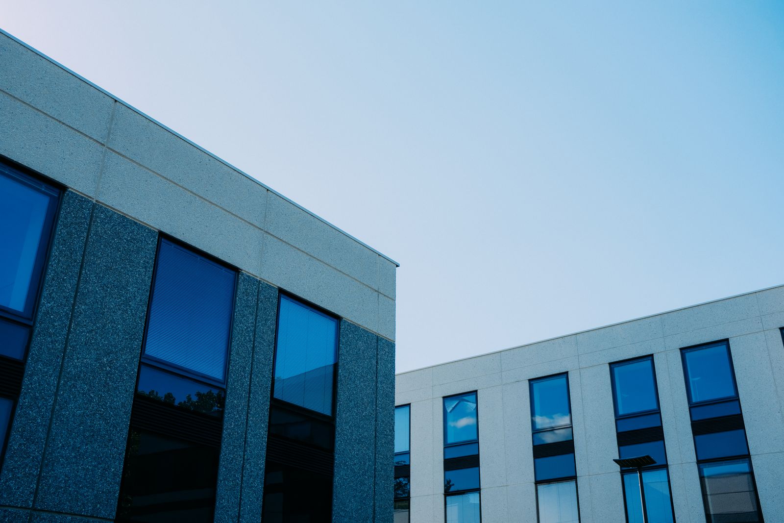 A modern commercial building of dark stone and blue glass, seen from below against a clear sky