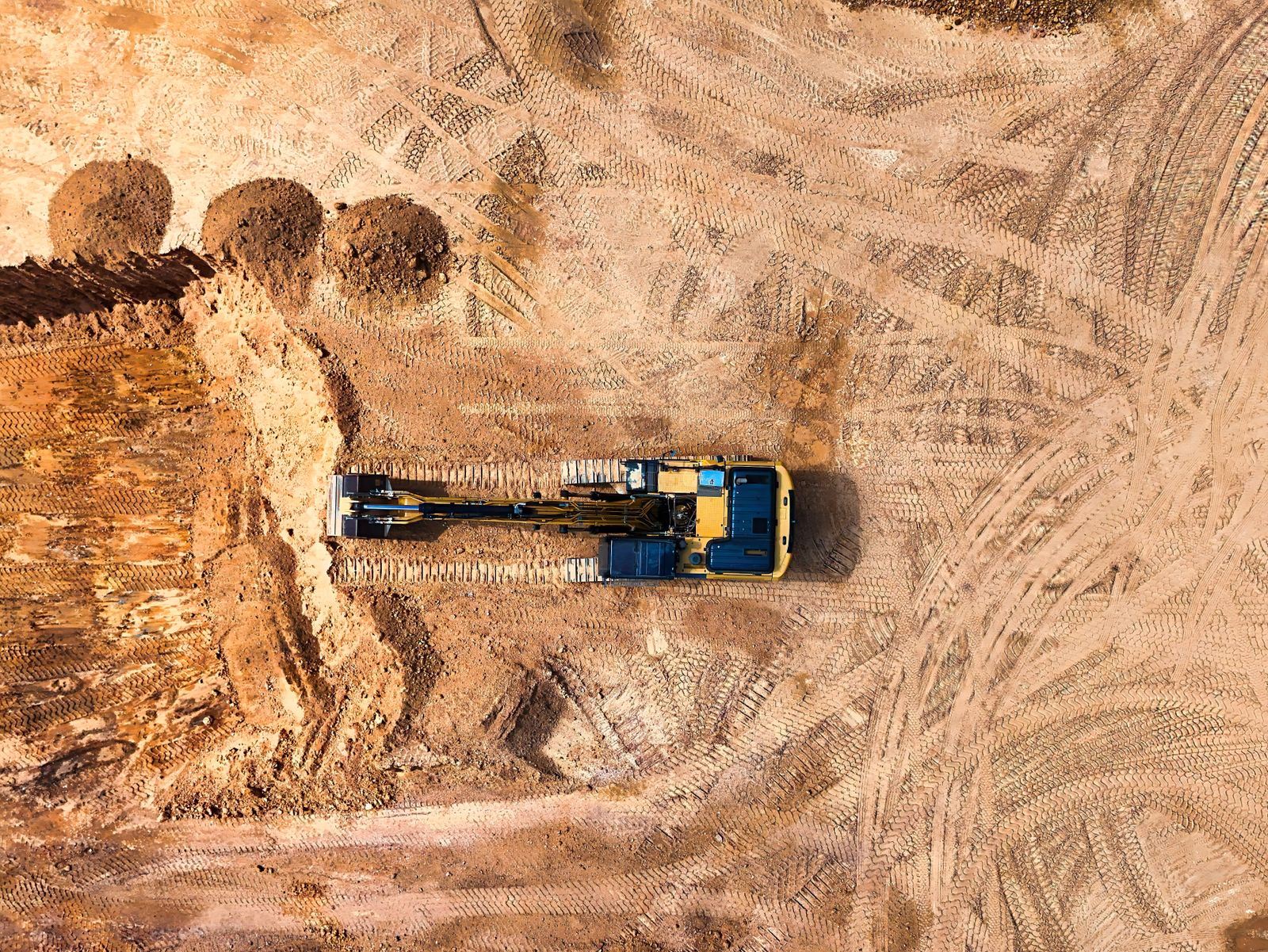 An aerial view of a tracked excavator cutting into an earth bank on a construction site