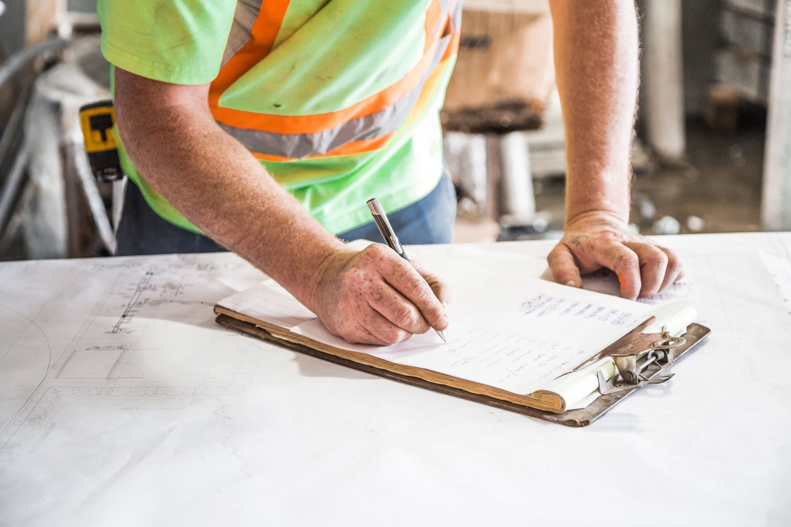 A worker in a hi-vis vest filling in a clipboard checklist inside an unfinished building