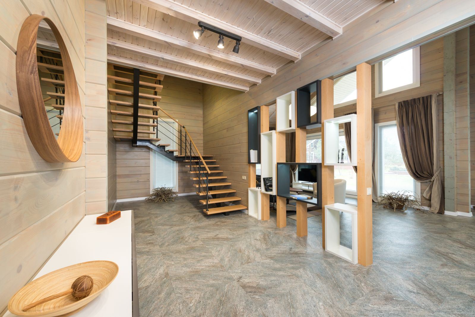A house interior with exposed pale wood ceiling beams, built-in shelving and an open wooden staircase